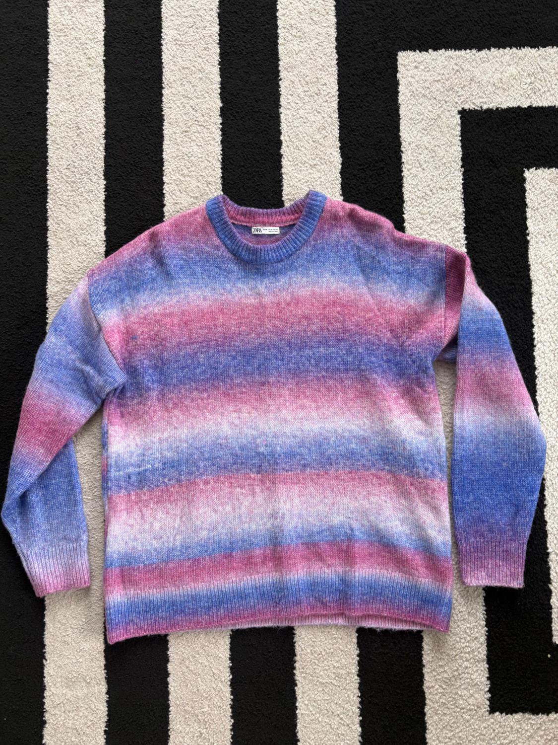 Horizontal striped sweater in shades of pink, blue, and white over a black and white geometric patterned rug.