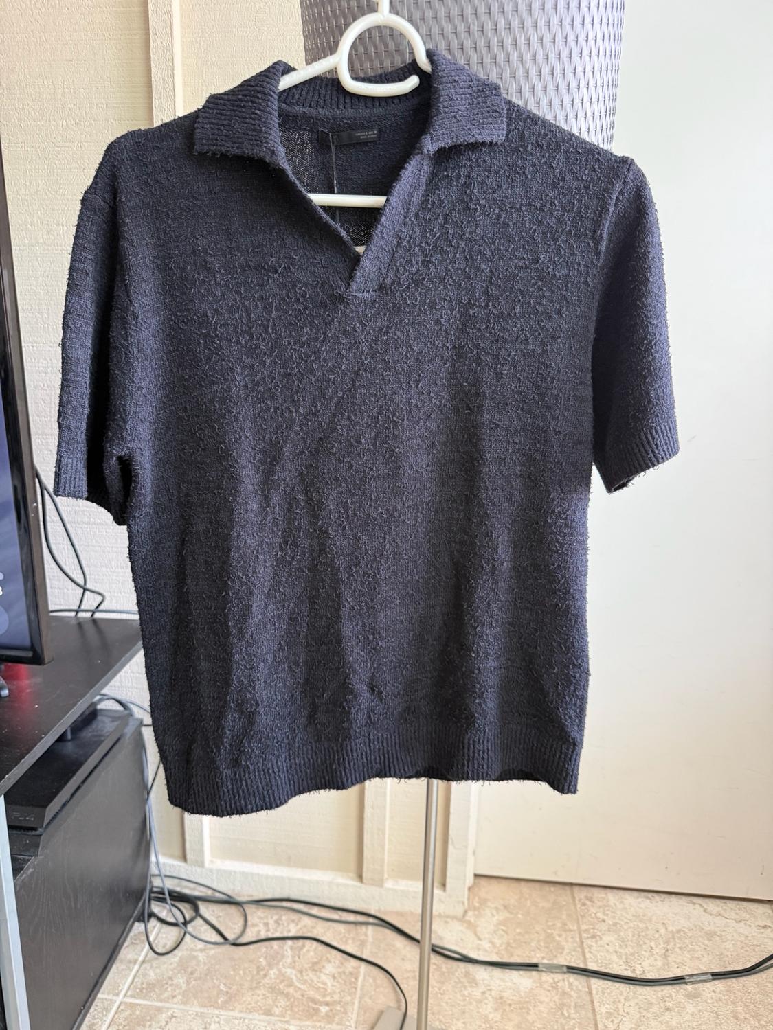 Dark blue short-sleeve polo shirt with textured fabric and a V-neck collar, hanging on a hanger in a room.