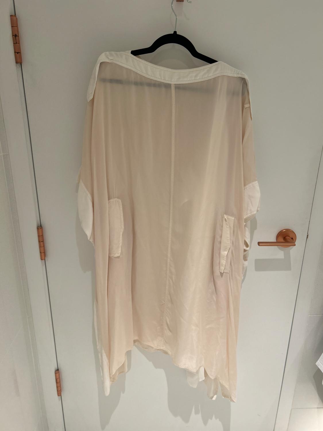 Translucent beige dress hanging on a black hanger over a white door. The light highlights its soft, flowing texture.