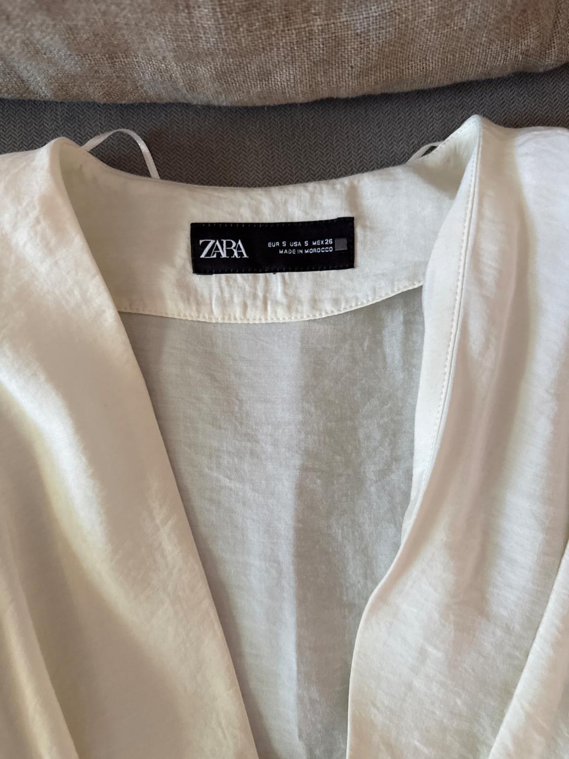 Label on a white Zara garment, size EUR S USA S MEX 26, made in Morocco, against a gray and beige fabric background.