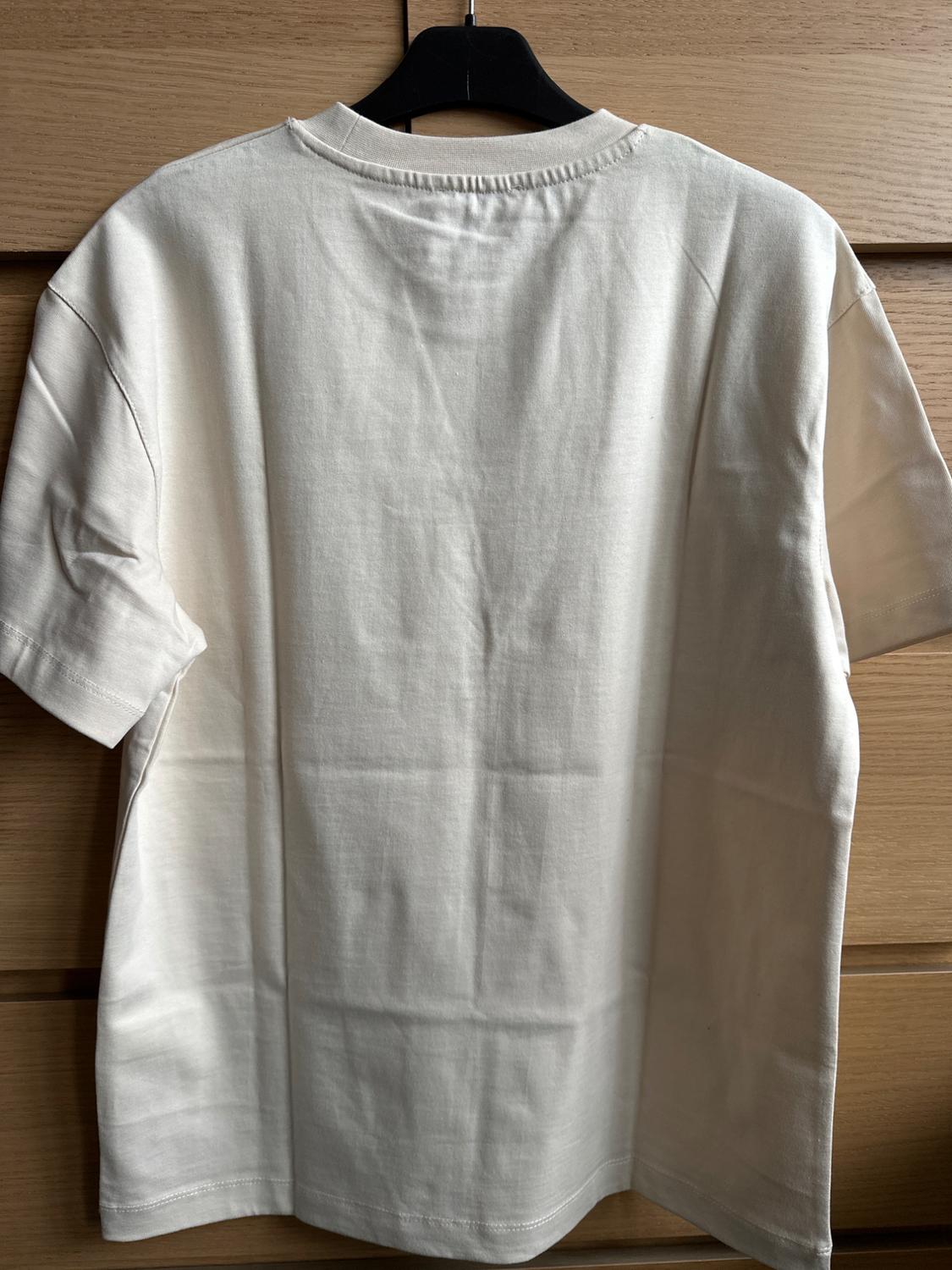 White short-sleeved T-shirt hanging on a black hanger against a light wooden background. Rear view of the garment.