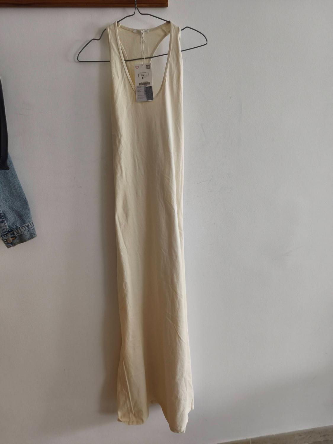 Casual cream-coloured strappy maxi dress hanging on a white wall. Part of a denim jacket is visible on the left.
