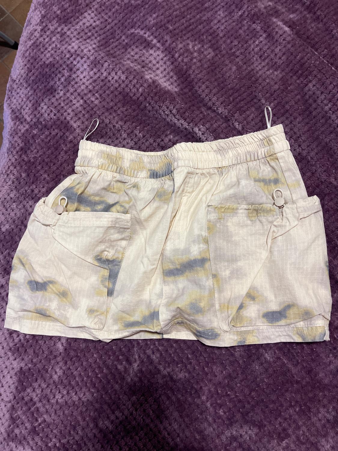 Light-coloured fabric shorts with a diffused grey and yellow print, on a textured purple blanket.