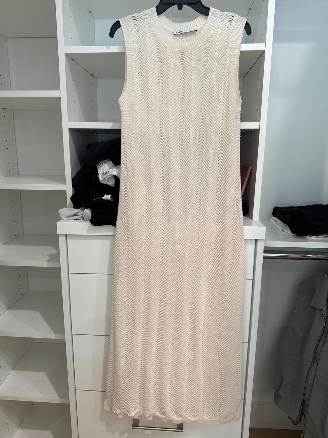 Sleeveless white dress with a wave pattern hanging in a white closet, surrounded by dark clothes and empty shelves.