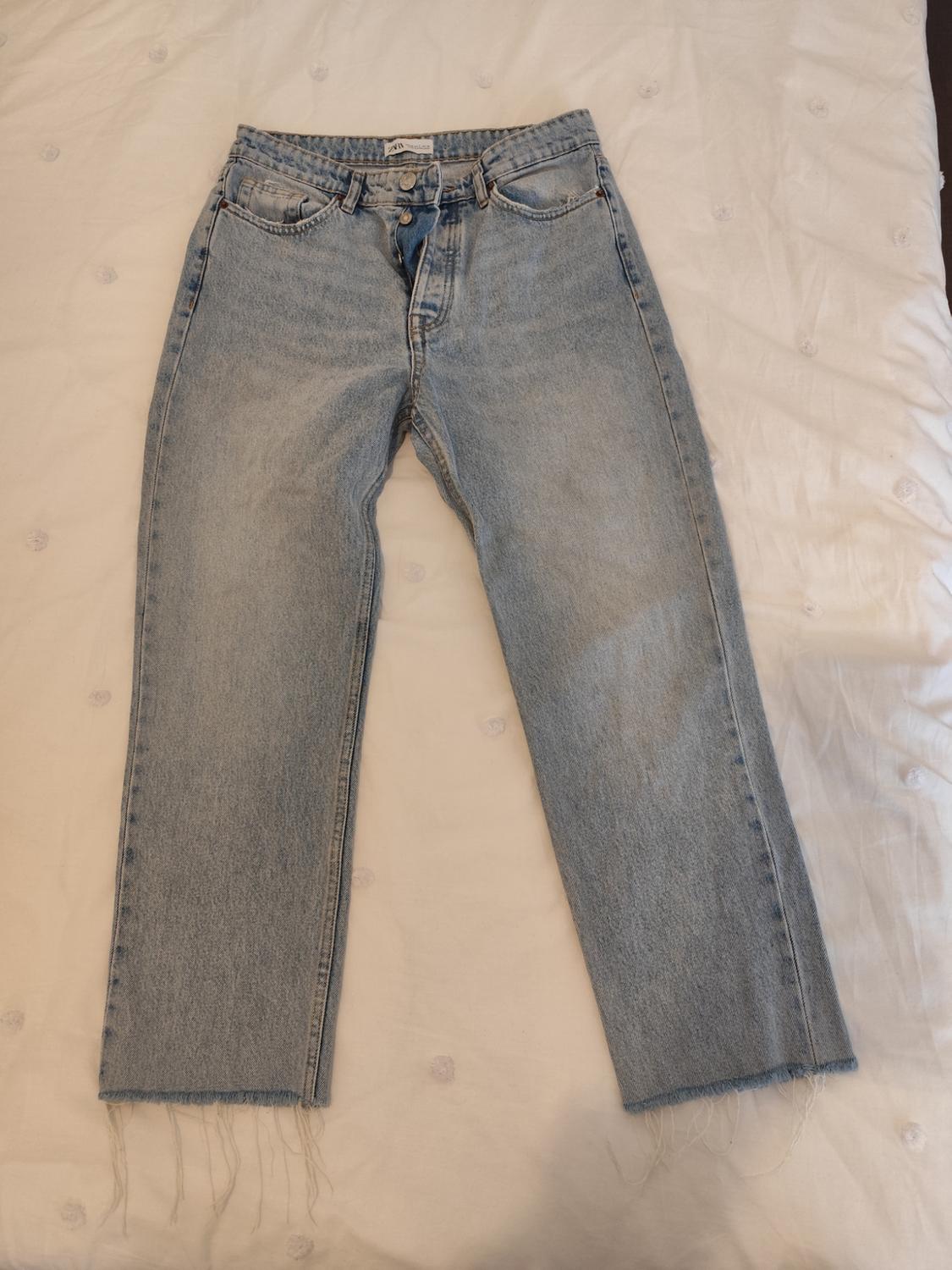 Light blue denim jeans with a frayed hem, placed on a white quilt with button details.