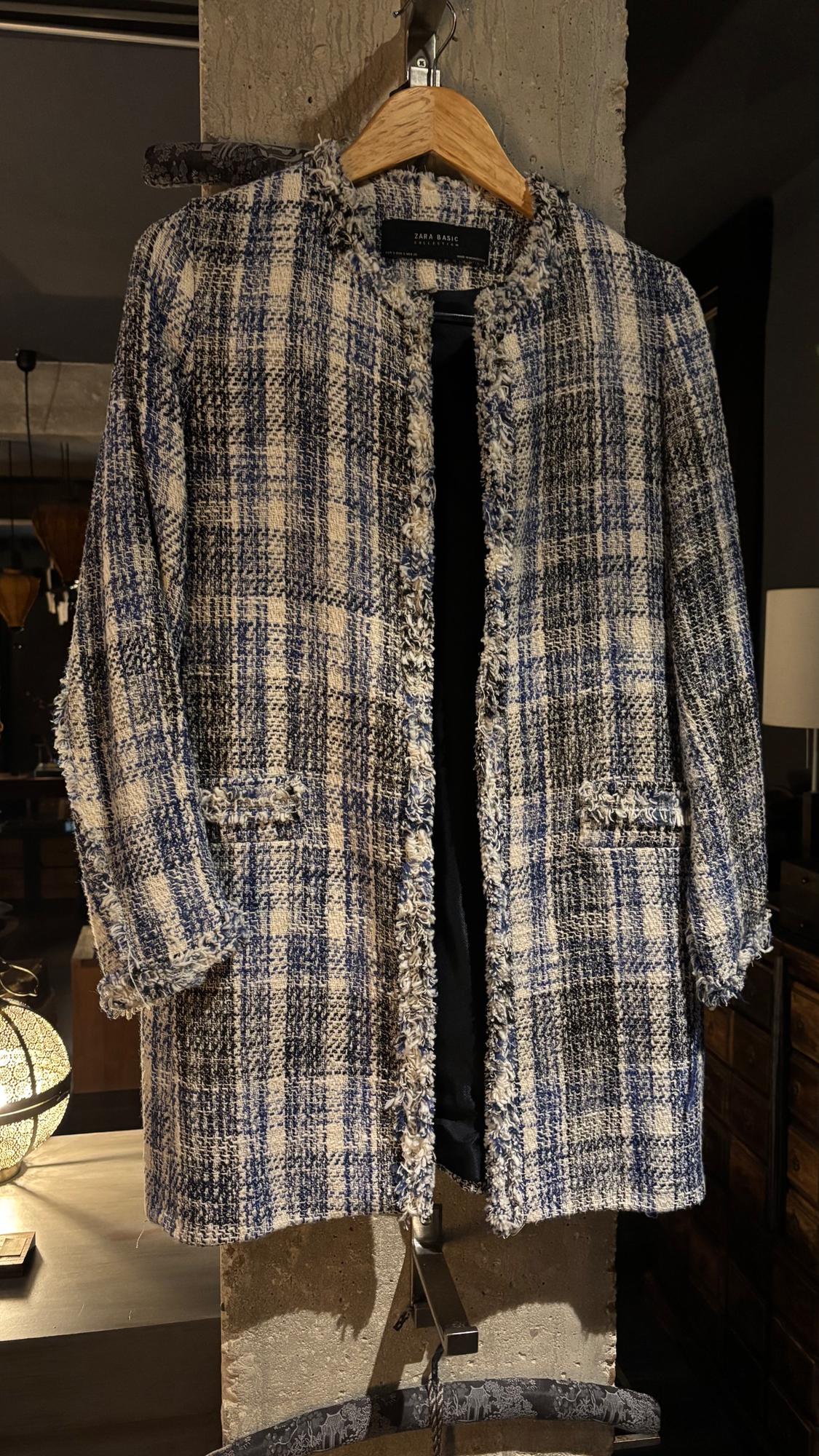 Blue and white checked coat hanging on a wooden hanger, with "ZARA BASIC" tag, in a warm indoor setting.