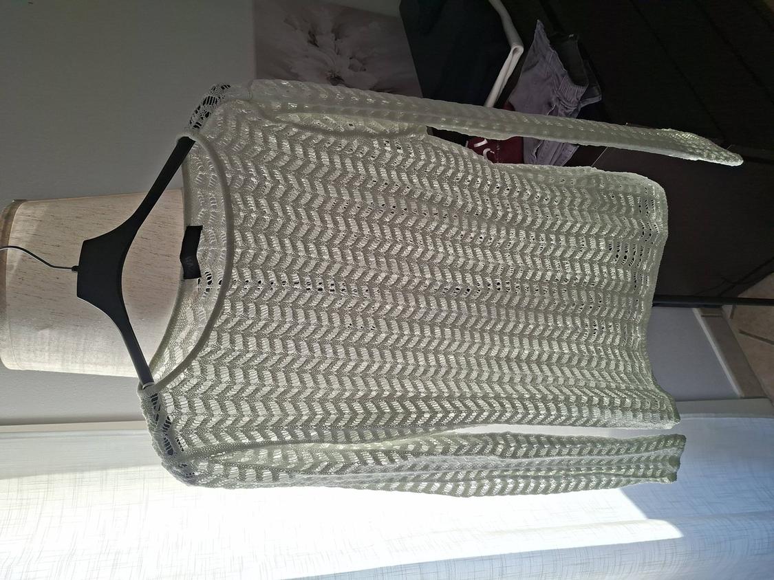 White knitted zigzag pattern jumper hanging on a wooden mannequin in a sunlit room.
