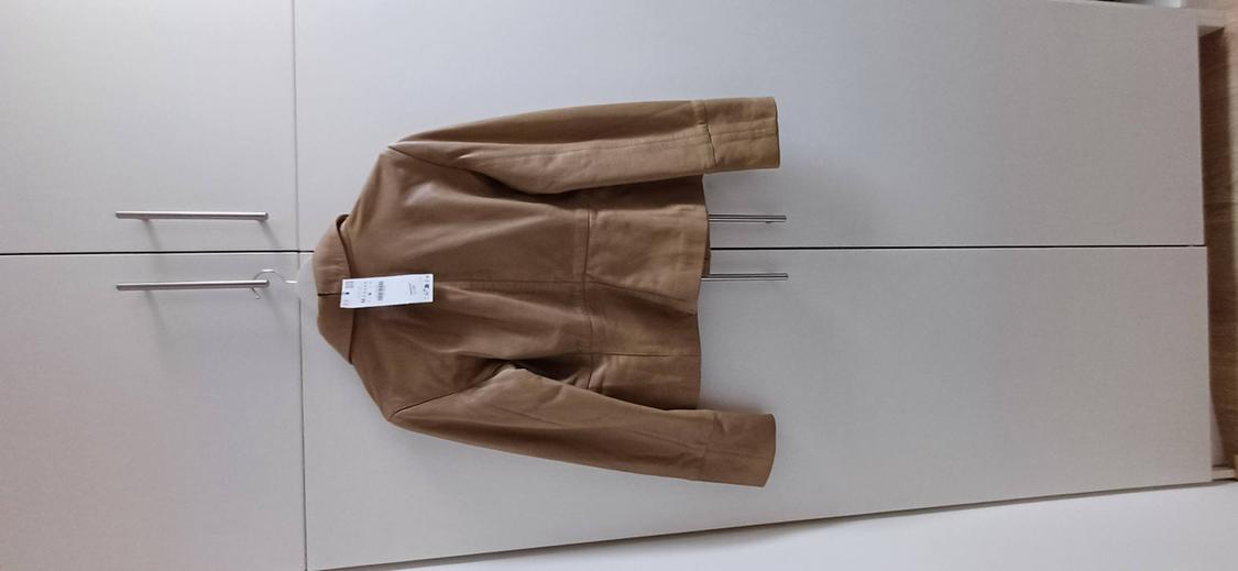 Brown jacket seen from the back with a label, hanging from the metal handle of a white wardrobe.
