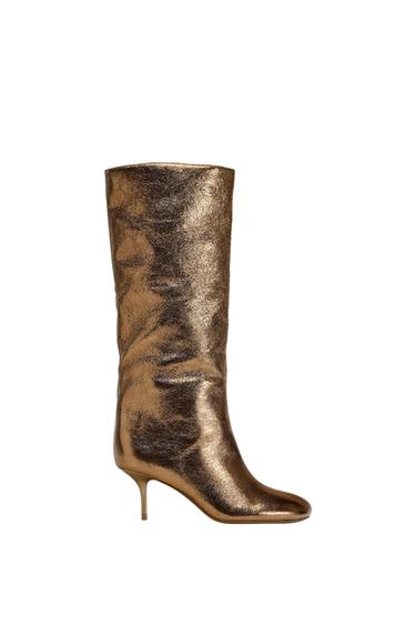 High boot with a thin heel in bright gold, with a wrinkled texture and elegant design on a white background.