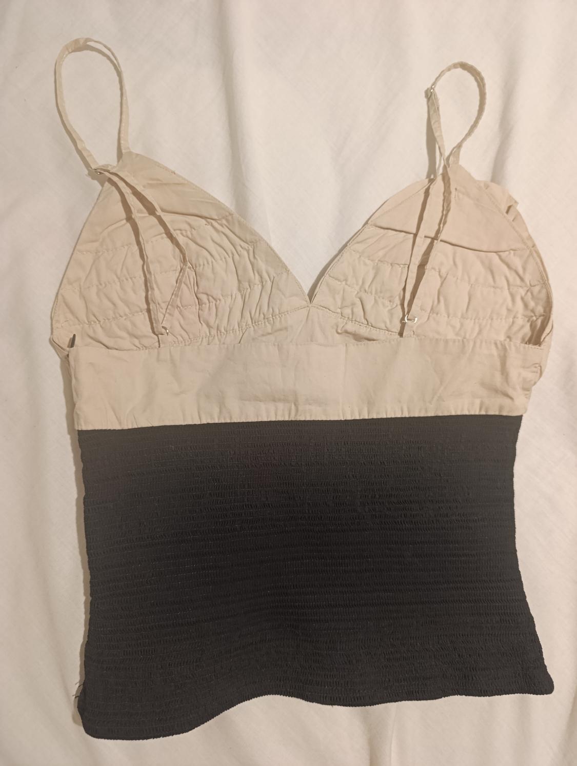 Beige and black camisole top on a white background. The upper part is beige with ruched cups and the lower part is black with a ribbed texture.