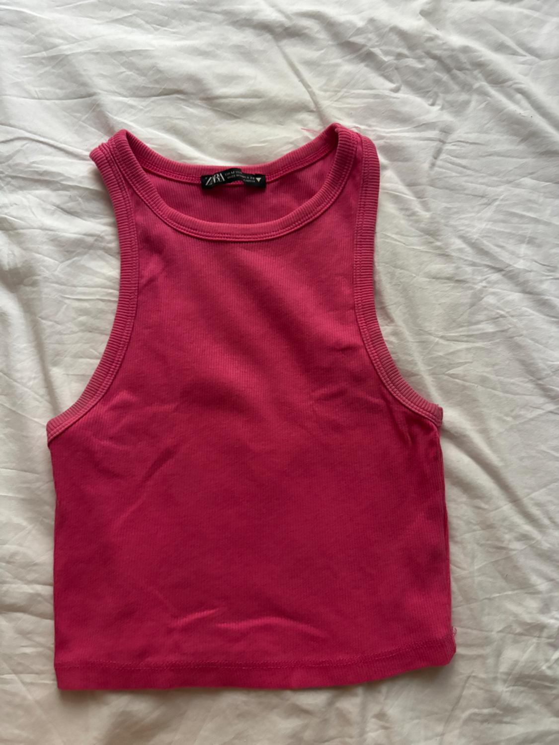 A pink sleeveless cropped top with a ribbed texture, laid out on a crumpled white sheet. The label reads ZARA.