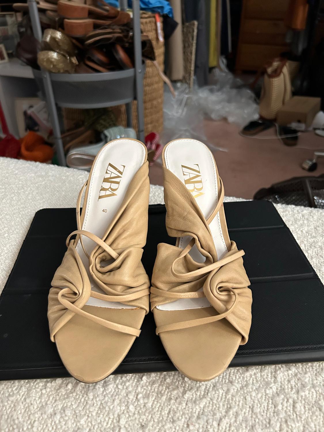 Front view of beige sandals with ruched design and visible logo on insole.