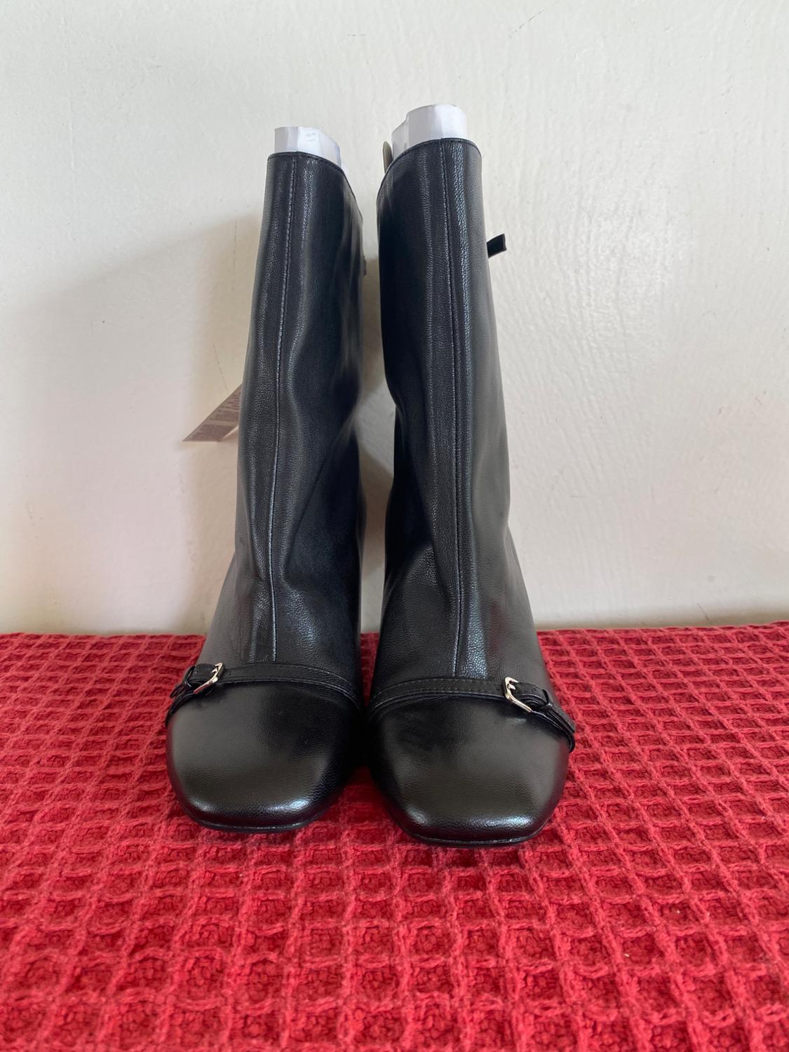 Black leather boots with square toes and metal buckles, on a red carpet with a checkered texture.