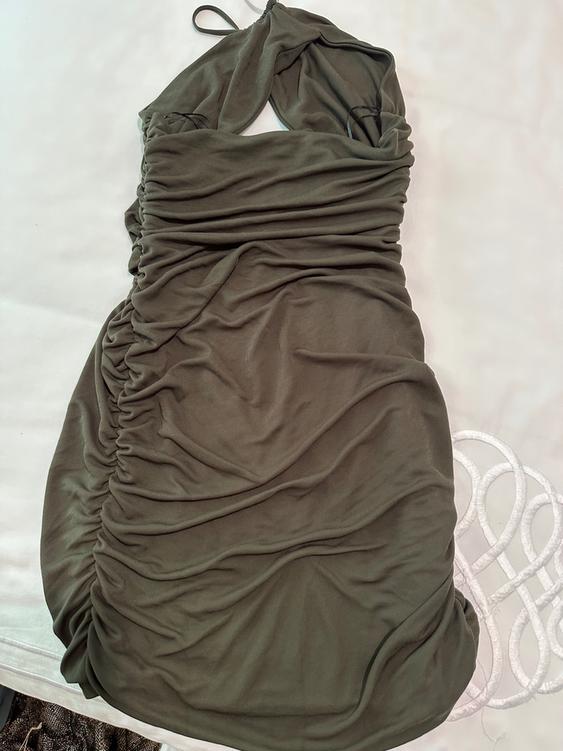 Olive green dress with draped design and thin straps, on a white surface with circular details in the background.
