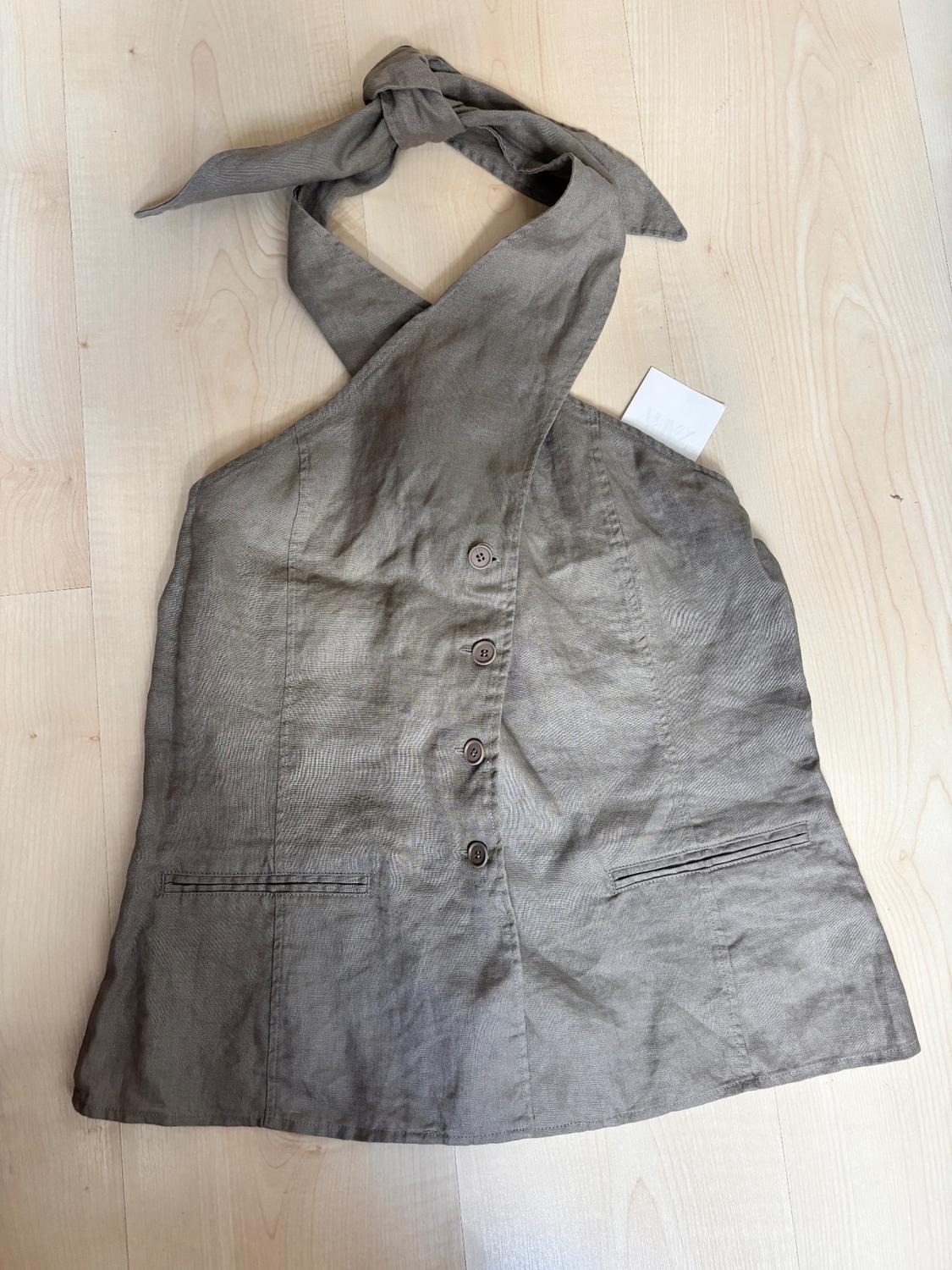 Grey sleeveless top with a knotted halter neck, front buttons, and faux pockets, on a light wooden background.