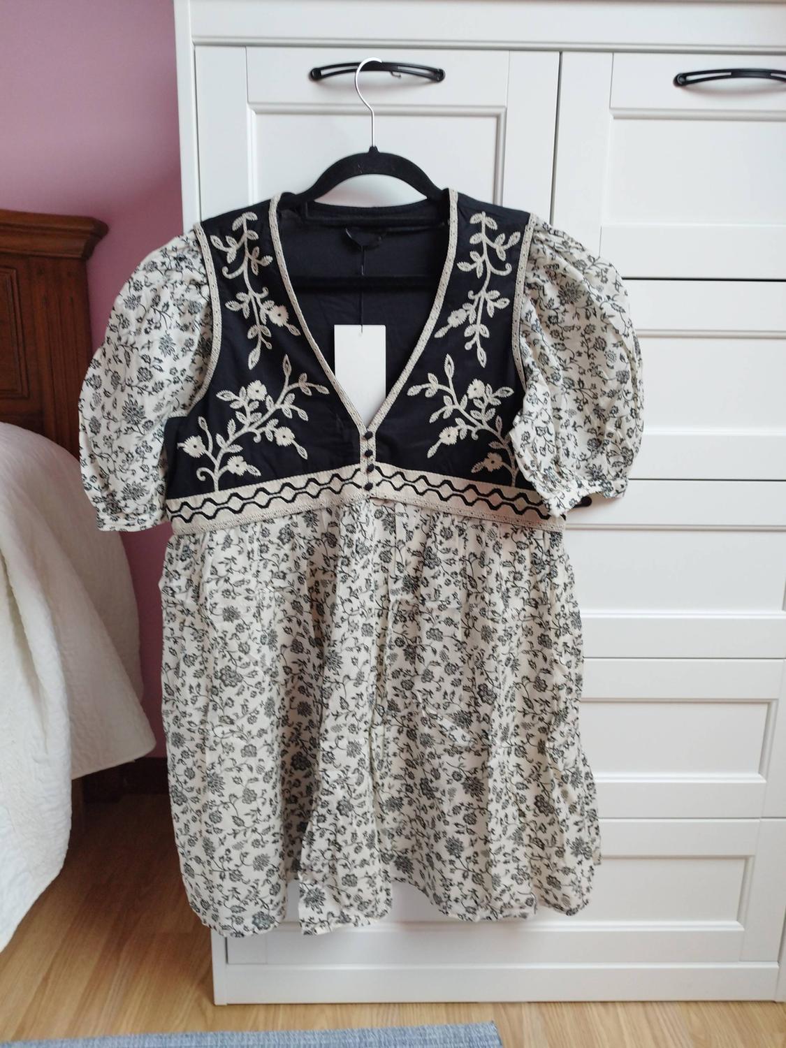 Dress hanging in a white wardrobe. Black bodice with floral embroidery, white sleeves and skirt with a floral print. Relaxed atmosphere.