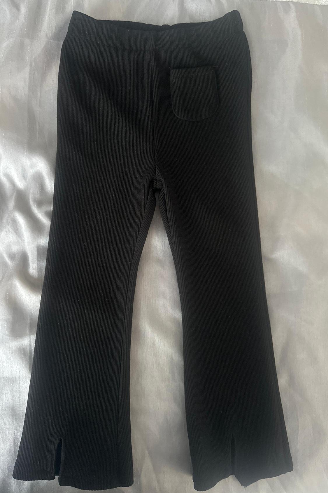 Rear view of black trousers with a back pocket and slits at the hems.