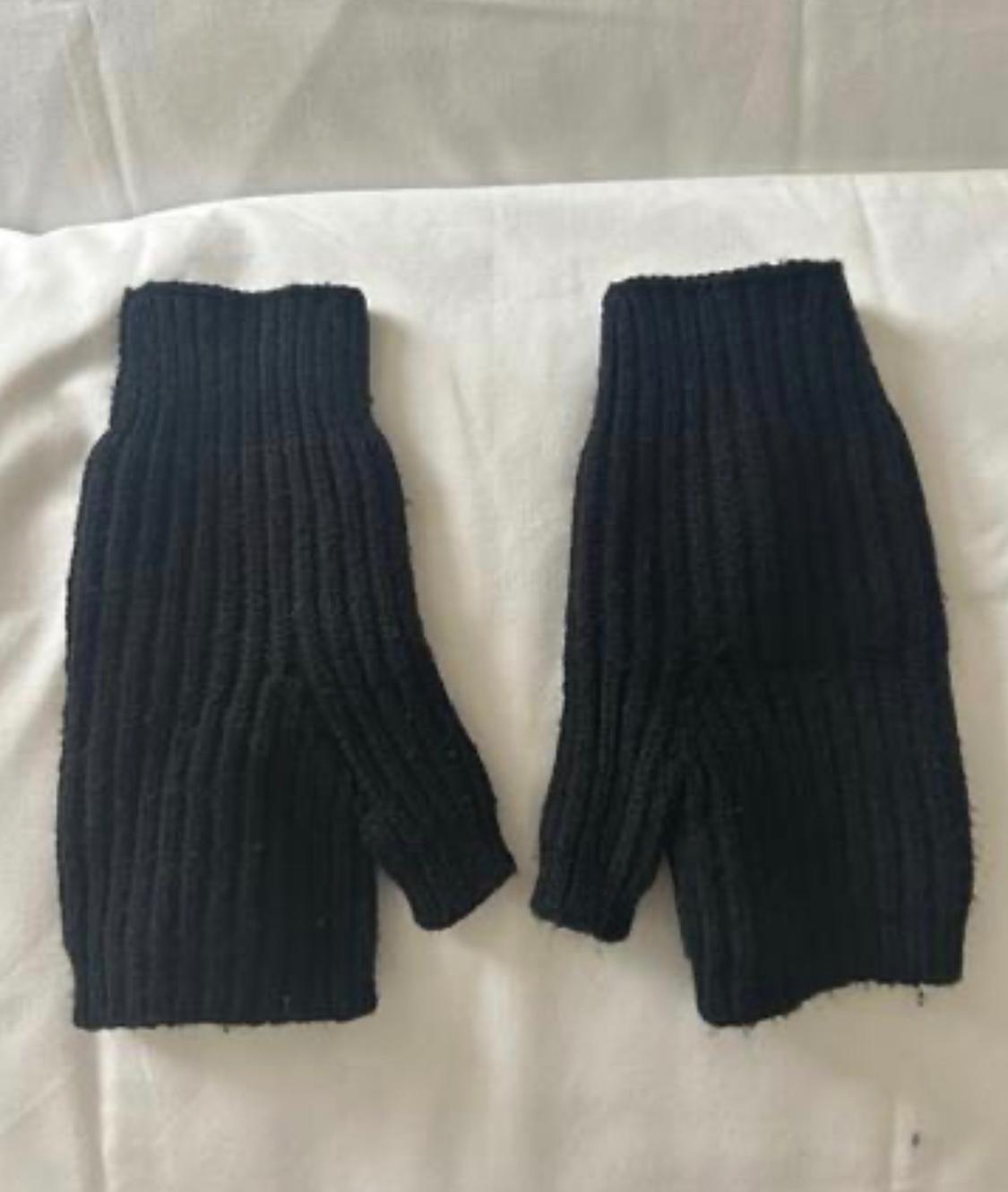 Pair of black ribbed knit fingerless gloves on a crumpled white fabric. Simple composition with a casual and relaxed style.