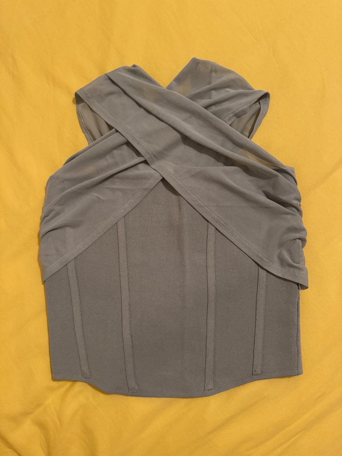 Sleeveless gray top with crisscross design on the upper part, on a yellow background. Textured fabric with vertical lines.
