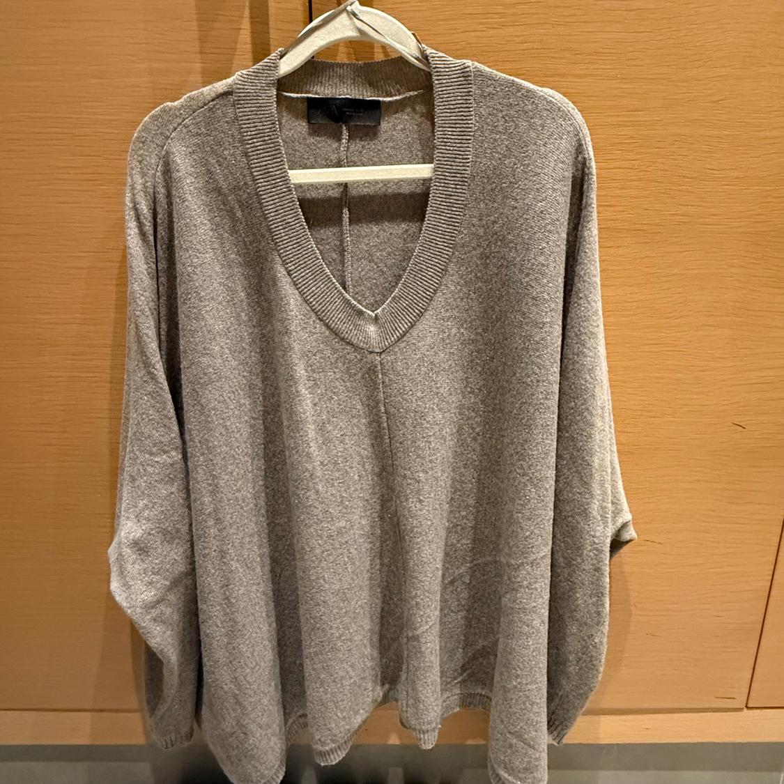 Grey knitted V-neck jumper hanging on a wooden hanger against a light wooden background.