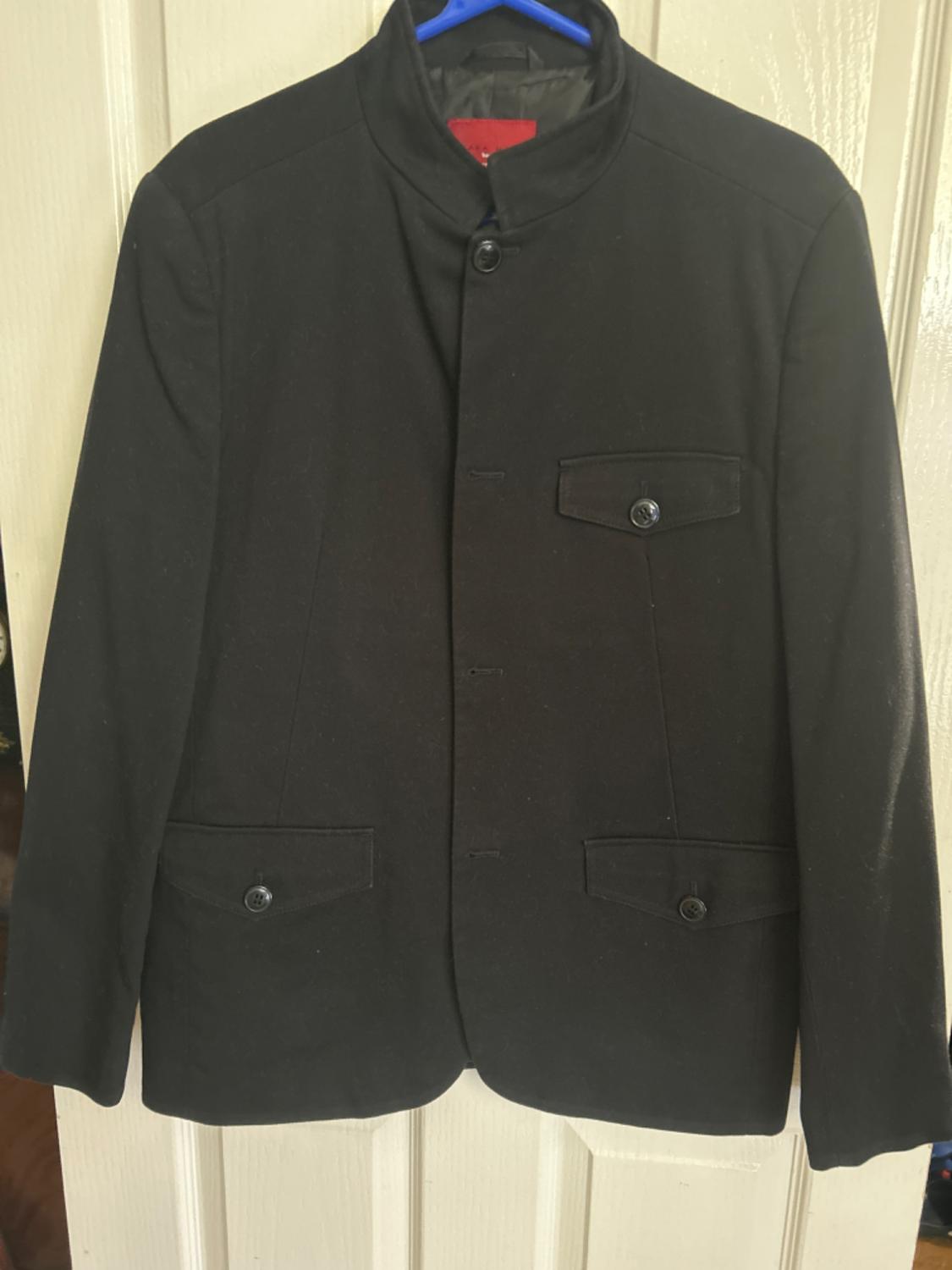 Front view of a black jacket with a high neck and front flap pockets with buttons.