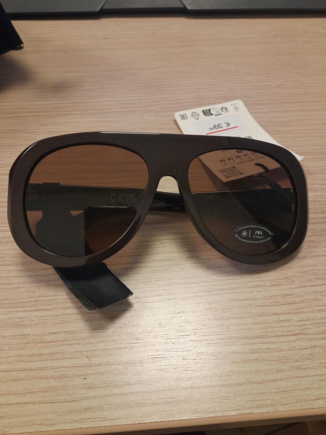 Brown sunglasses on a wooden table. Texts: "€ 39.95", "SIZE", "CE UK CA", "ZARA" and "Category 3".