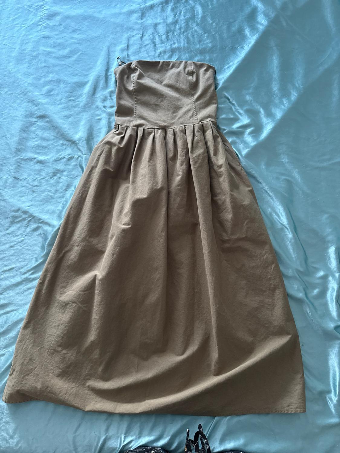 Beige strapless dress with a gathered skirt, photographed from above on a shiny, wrinkled light blue fabric.