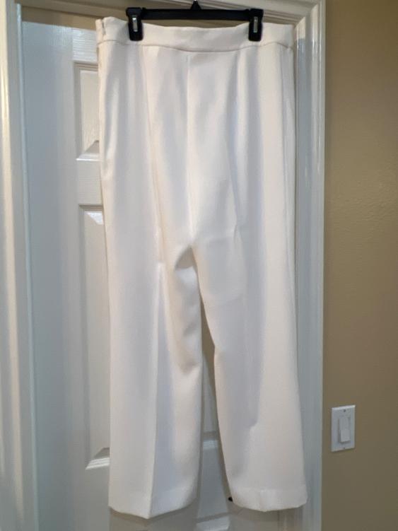 White pants hanging on a black hanger over a white door. Beige wall background and dim light.