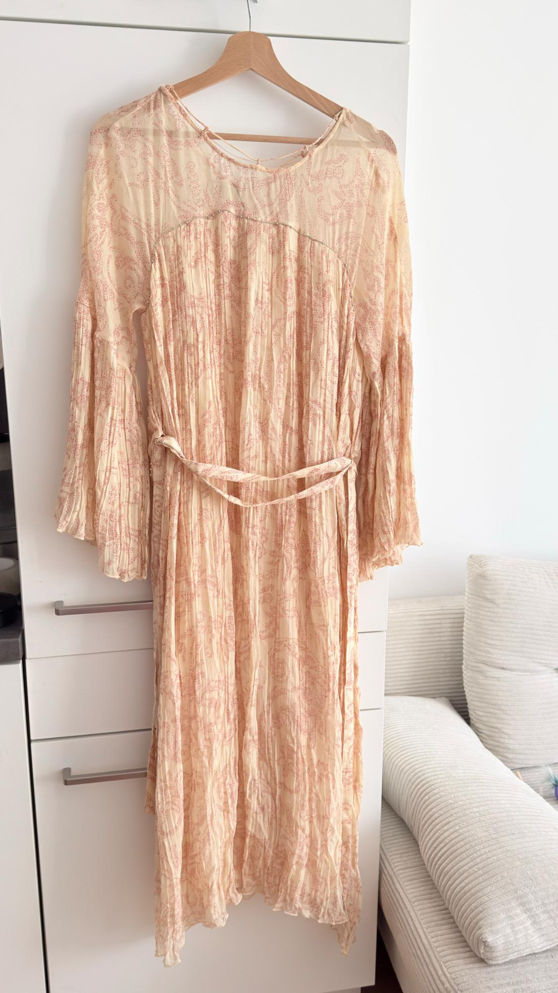 Beige dress with a pink floral print, long sleeves and a belt, hanging on a hanger against a white wardrobe background.
