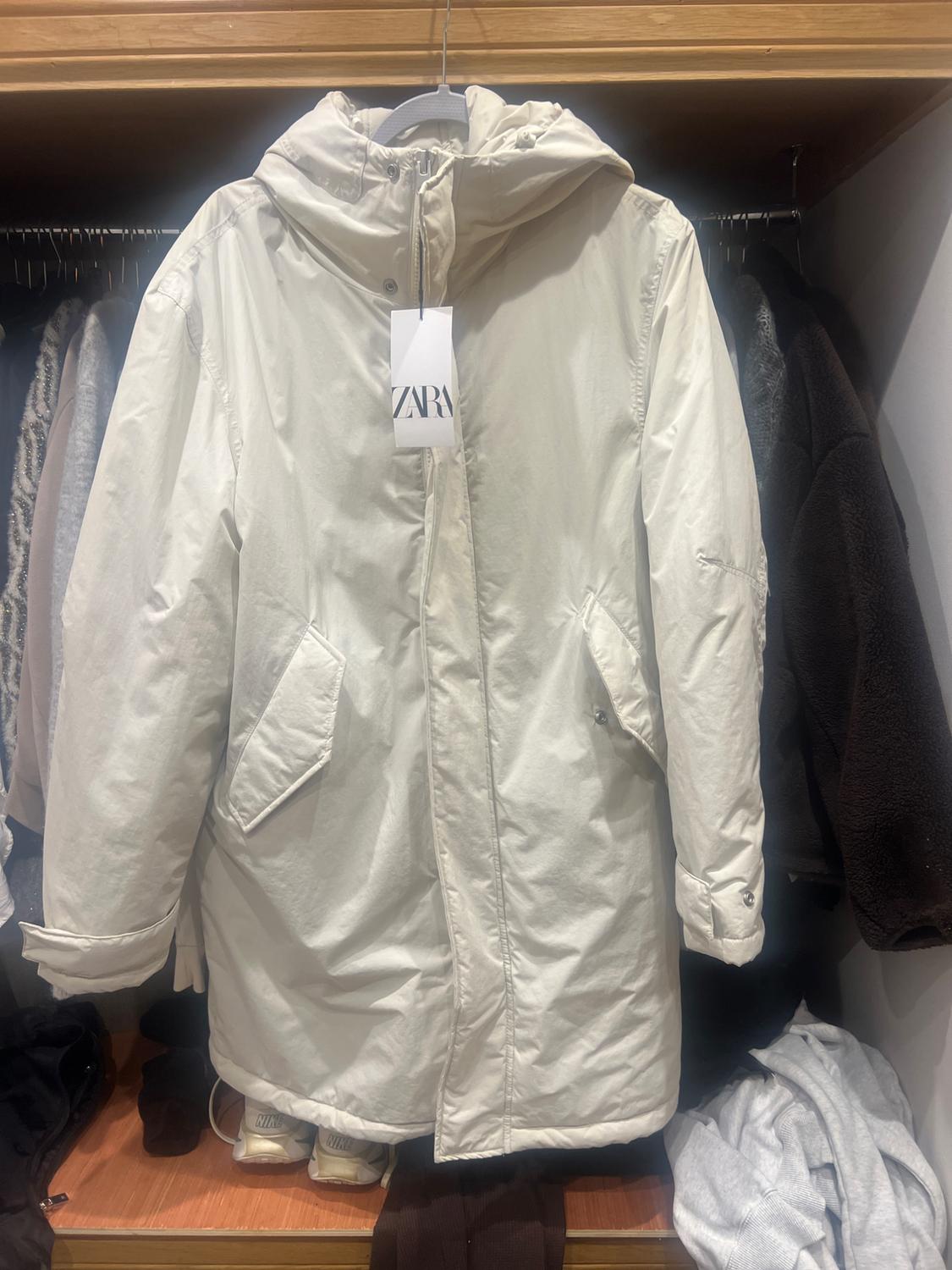 White hooded coat hanging in a wardrobe, visible label with the text "ZARA". Clothing and footwear on the bottom shelf.