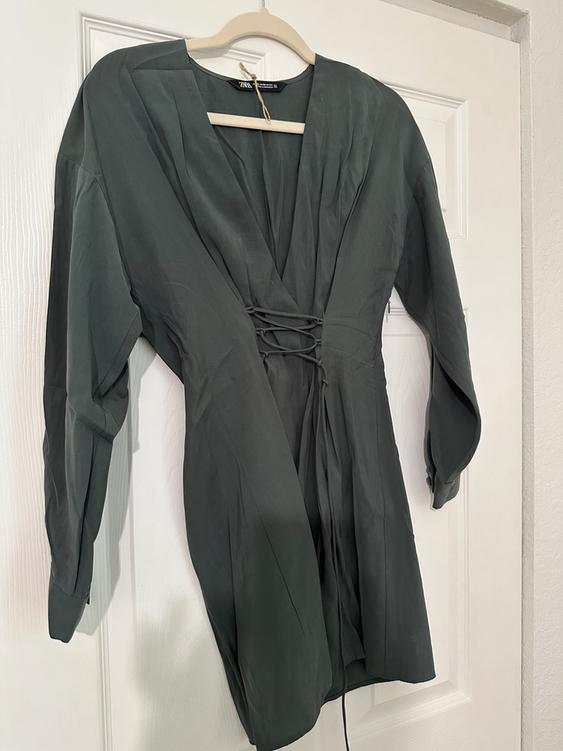 Dark gray dress with a V-neck and waist ties, hanging on a wooden hanger over a white door.