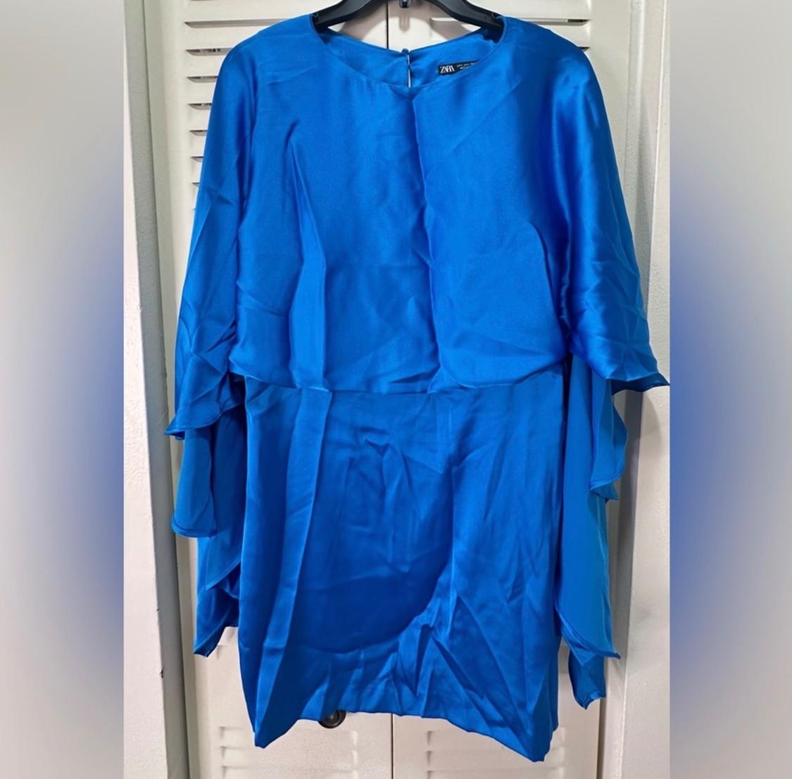 Bright blue dress hanging on a hanger, with loose sleeves and a flowing design. White doors in the background.