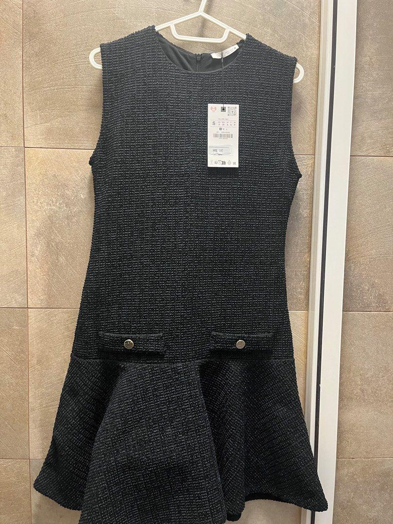 Sleeveless black textured dress hanging on a white hanger. Visible tag with product details. Beige tiled background.
