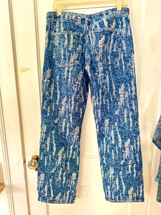 Blue denim jeans with a distressed white print, hanging on a hanger in front of a white door.