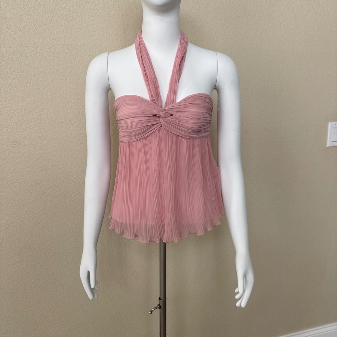 White mannequin wearing a pink pleated halter-neck top with a knotted detail at the chest, in front of a plain beige wall.