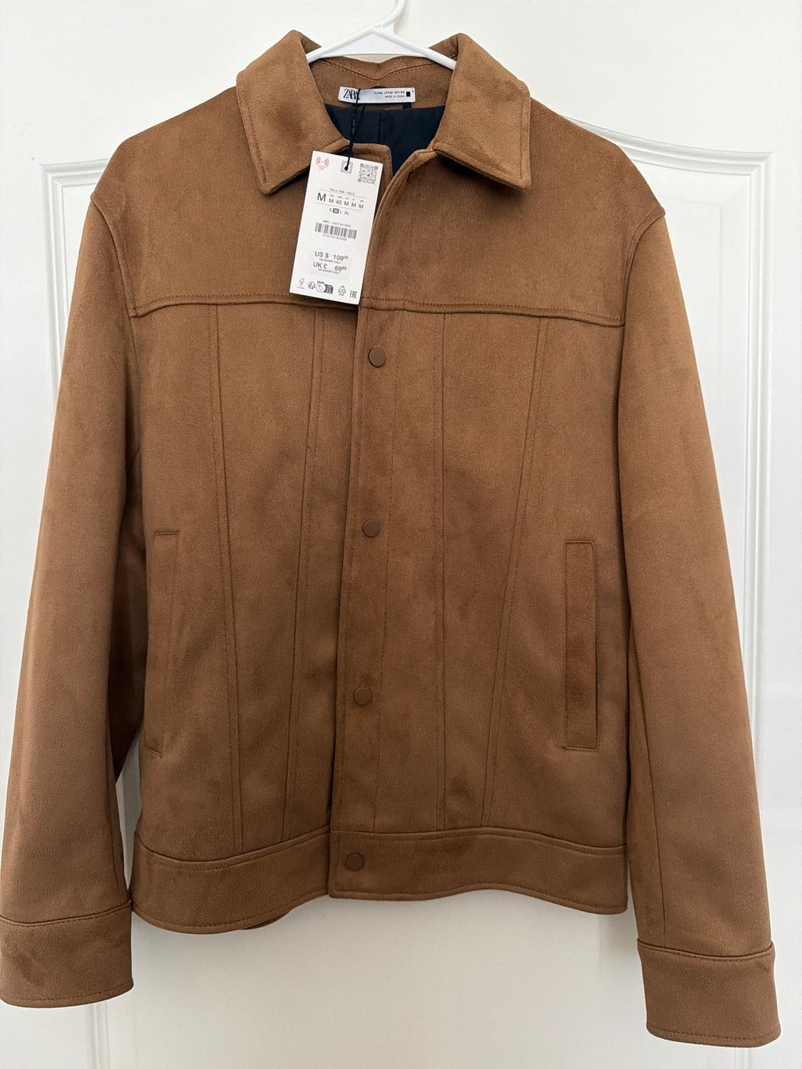 Brown jacket hanging on a white hanger, with a visible tag showing size M and a price of $109. White door background.