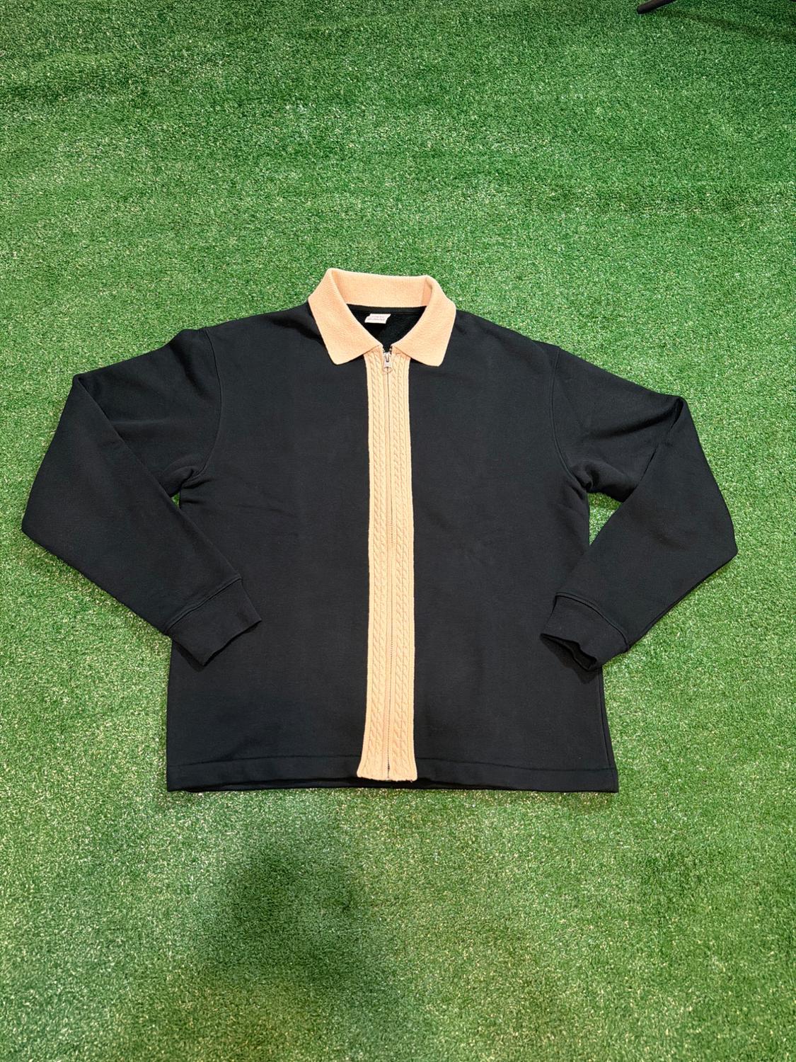 Black jacket with zipper and beige collar, on green grass.