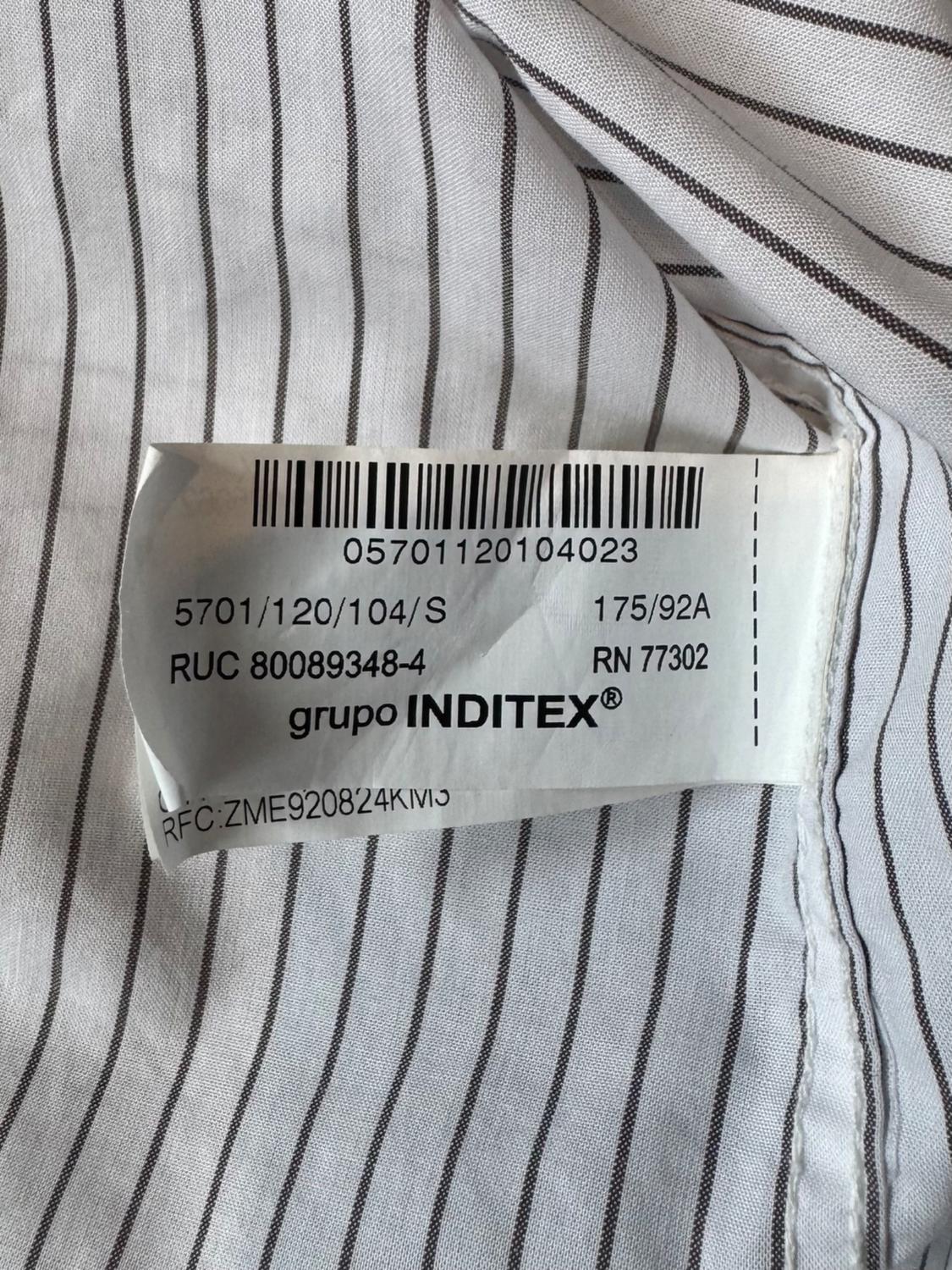 White clothing label with black stripes, displaying barcodes and text: "grupo INDITEX", "RUC 80089348-4", "RN 77302".