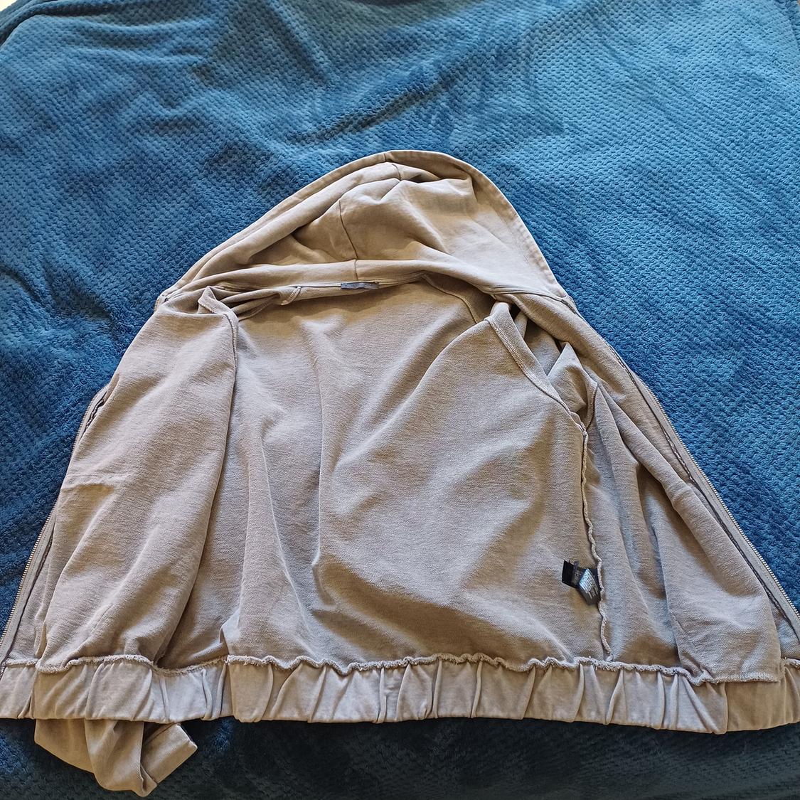Beige jacket with a hood spread over a textured blue blanket. The jacket has a simple, casual design.