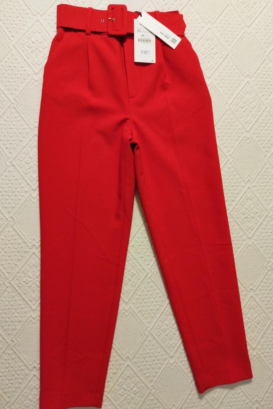 Front view of red trousers with belt and visible labels.