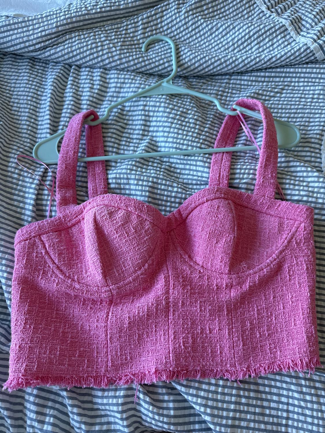 Pink textured crop top hanging on a green hanger against a grey and white striped fabric.