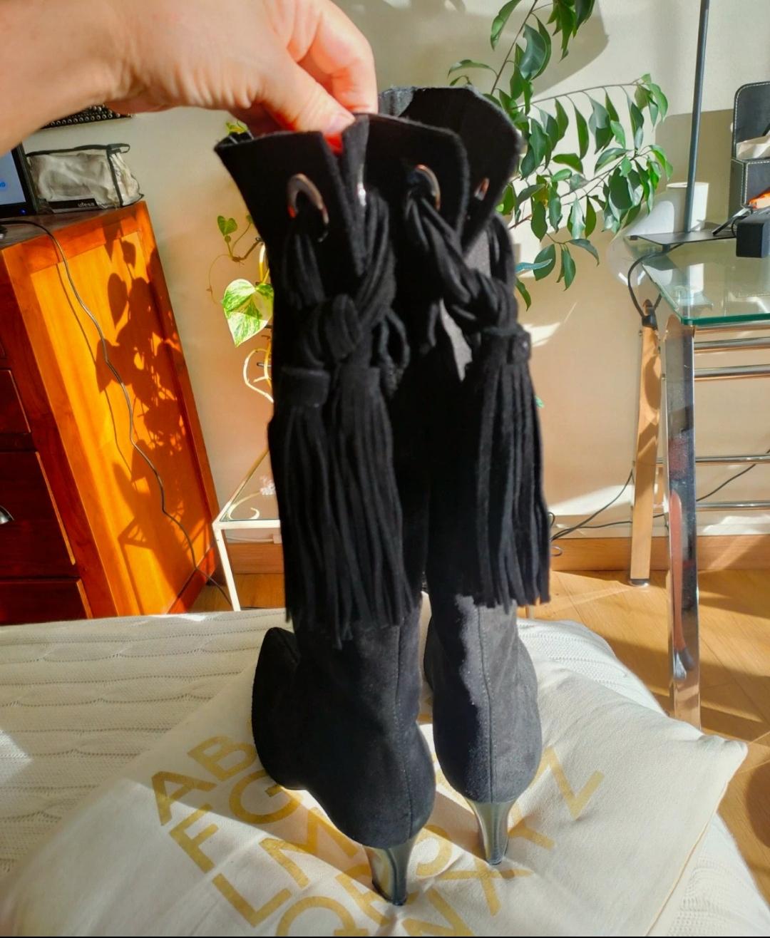 Rear view of black boots with a metallic heel and decorative tassels.