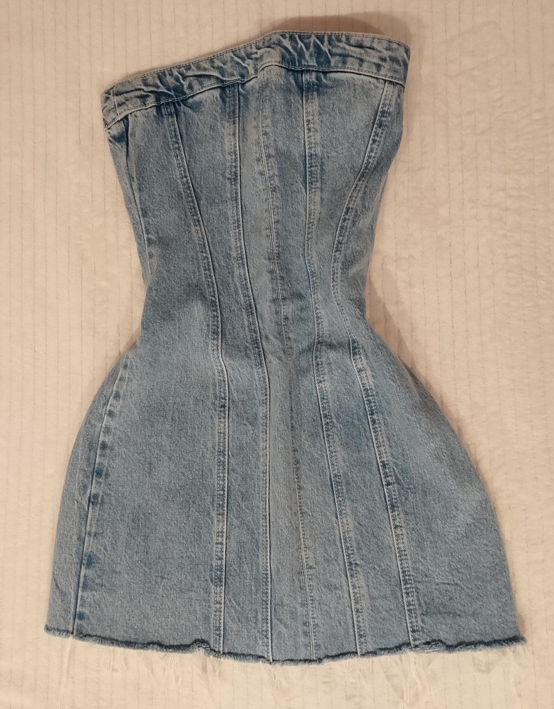 Light blue strapless denim dress with vertical seams and a frayed hem, laid out on a textured fabric background.