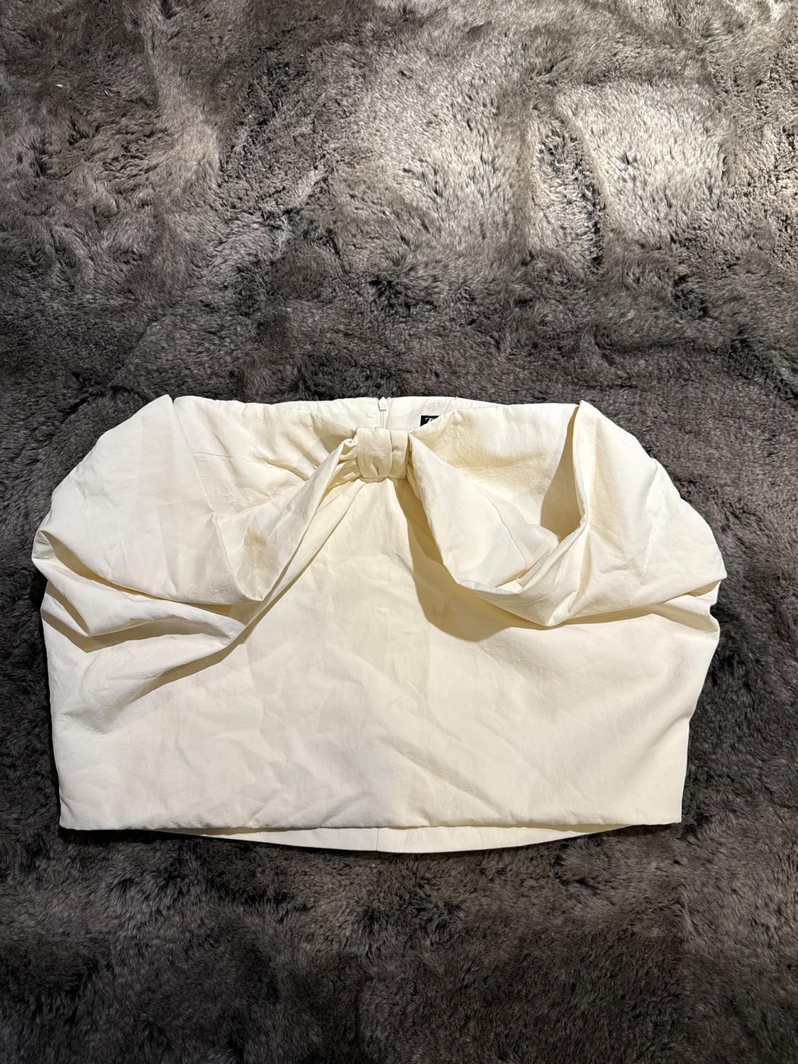 White bag with a bow design on a fluffy gray rug. The bag has a wrinkled and elegant look.