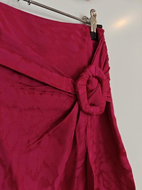 Red skirt with floral texture and waist knot detail, hanging on a metal hanger against a white background.