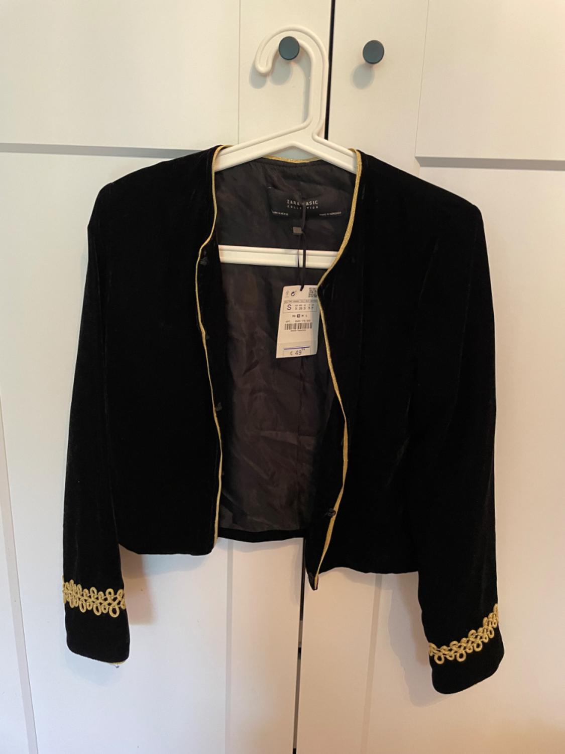 Front view of a black jacket with gold trim and embroidery on the cuffs.