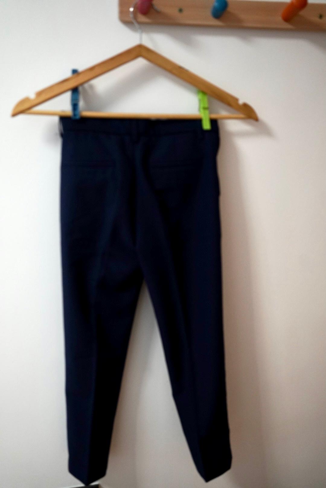 Dark blue trousers hanging on a wooden hanger with colourful pegs, against a white wall.