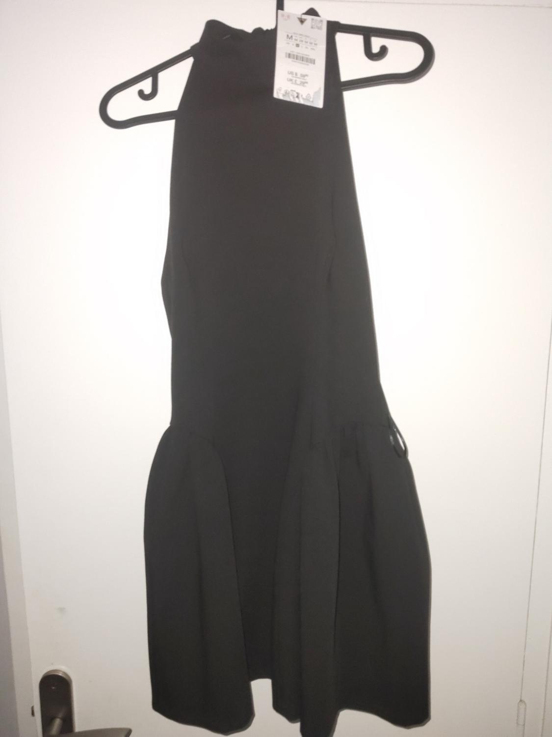 Sleeveless black dress hanging on a black hanger, with visible tag, on a white background.