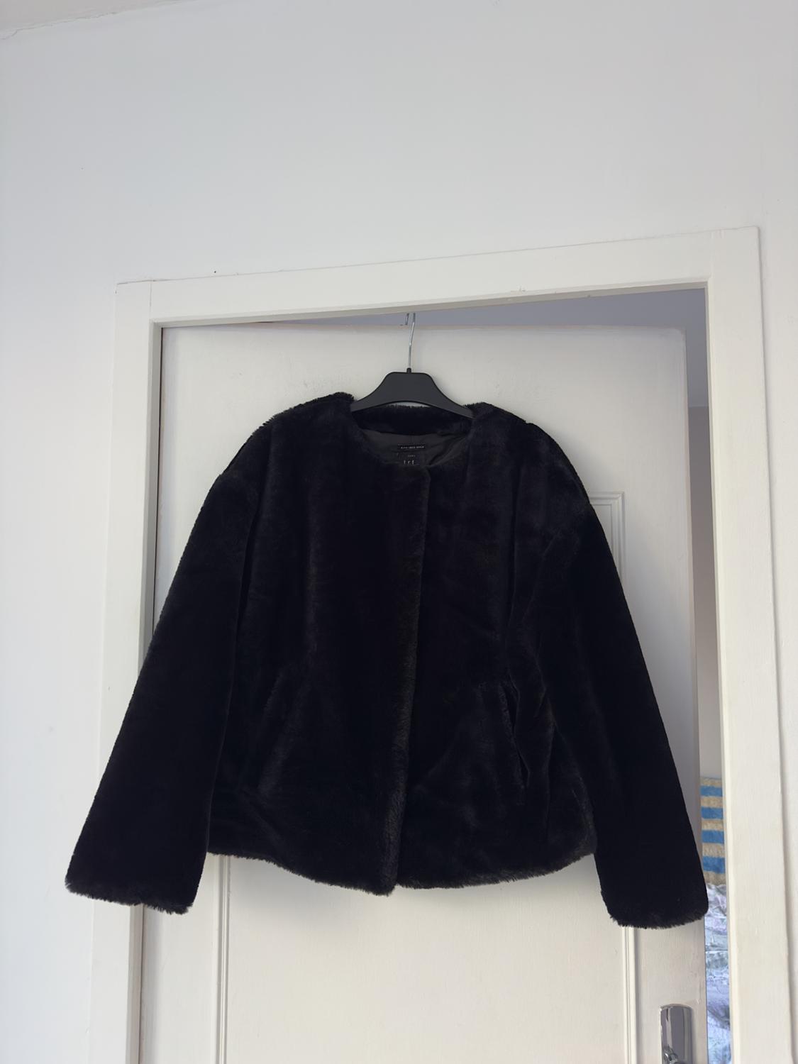 Black faux leather jacket hanging on a white door. The jacket has a simple and elegant design.