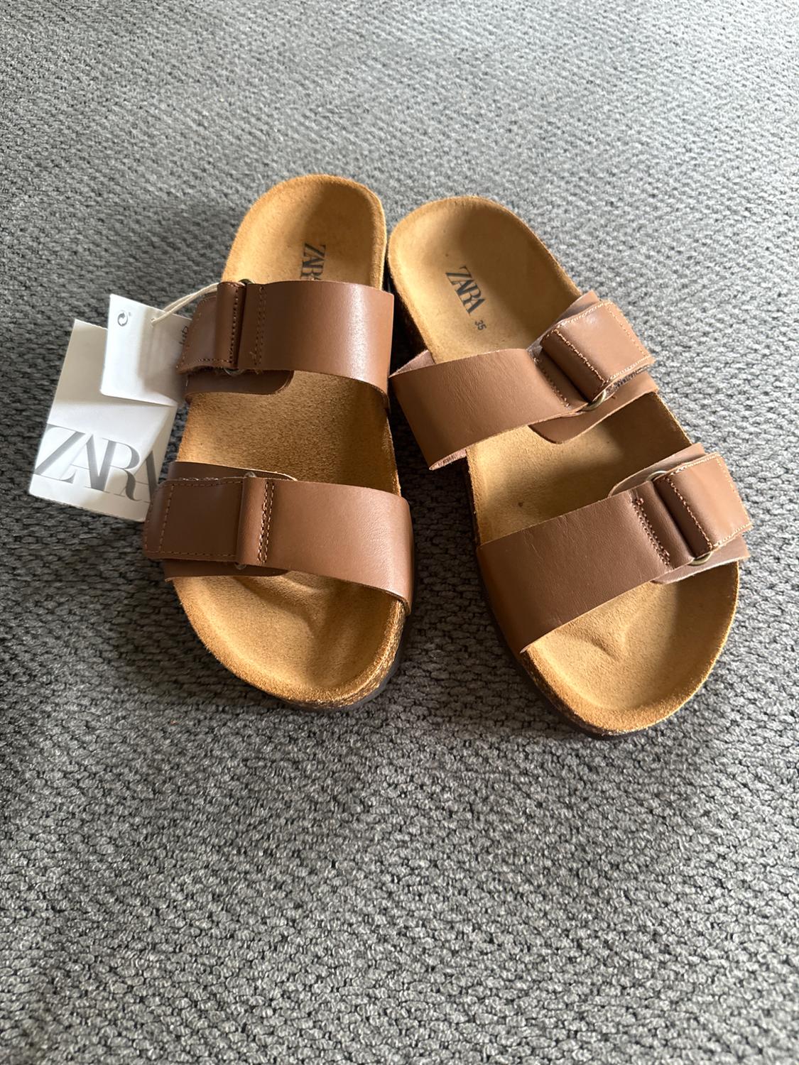 Front view of brown sandals with double buckle and visible label.